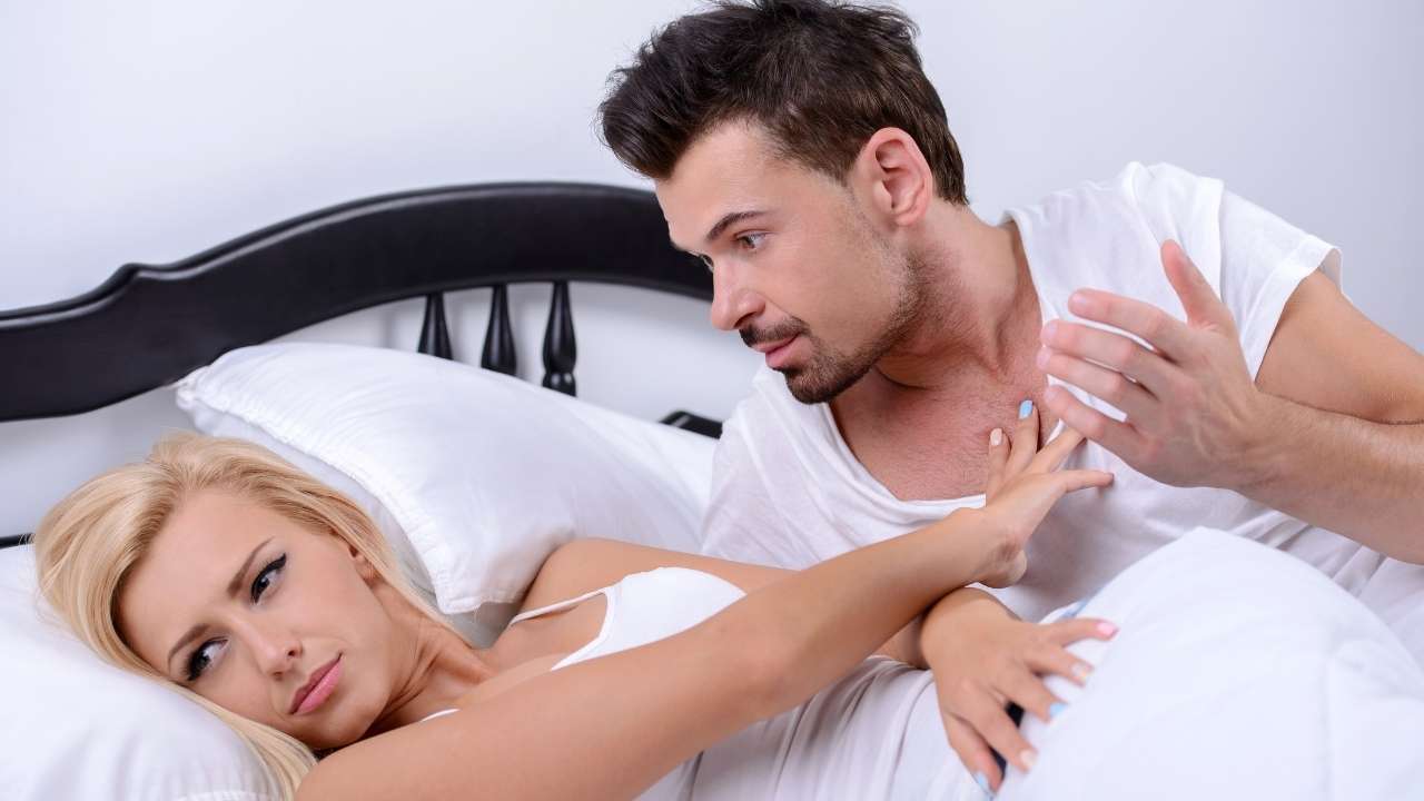 Парень в серой майке лежит на кровати и дает блондинке с большими дойками пососать пенис